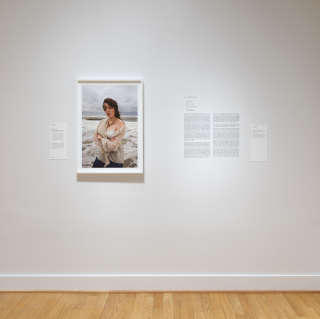 White gallery wall hung with a framed photo of a woman on a beach and accompanying text.