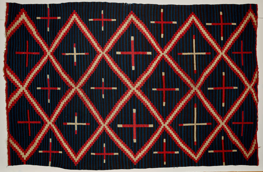 Striped navy blue blanket with three, different sized, alternating cross patterns: red crosses, red with white tips, and white with red tips, within a red and cream three-striped diamond pattern.
