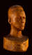 Three quarter front view of a wooden bust depicting the head of a male figure with afrocentric facial features. His expression is stern and holds an intense gaze.