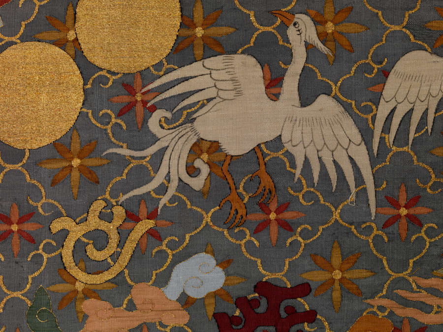 Detail of the gray-blue robe’s back, featuring  a golden diagonal grid pattern with floral motif overlaid with white birds, golden circles and symbols with wispy earthy-pastel clouds.