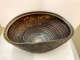 Partial top-view of an oblong bowl with circular ridges on the inside. The outside of the bowl has shell-like etchings and sides that dip to form a wave-like shape. 