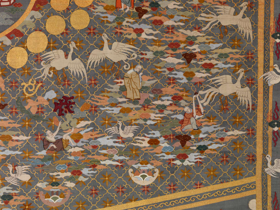 Detail of the bottom-right quarter of the robe’s back, featuring densely-packed illustrations of white birds, earthy-pastel clouds, robed priests, golden symbols and floral motifs against a background of layered patterns.