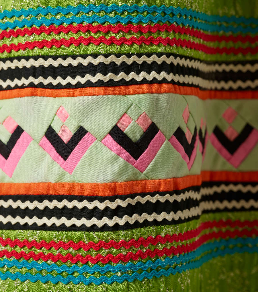 Another detail of the pattern. A thick strip of off-white with pink and black rectangles woven through it is surrounded by wavy horizontal red, blue, green, white, and purple stripes. 

