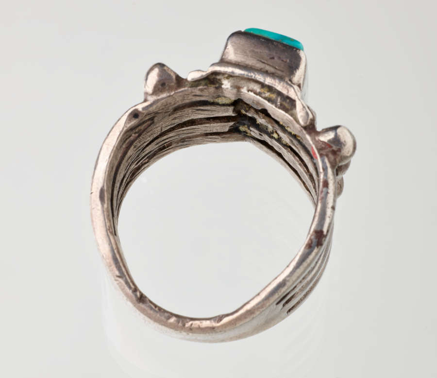 Top-view of a silver metal ring with a turquoise stone-setting. Visible are the inner grooves flowing across the band’s interior and towards the stone.