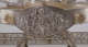 A close-up of a silver oval relief panel depicting a robed man surrounded by cherubs, vines, and swirling drapery, enclosed in a gold-trimmed frame attached to an elevated tray.