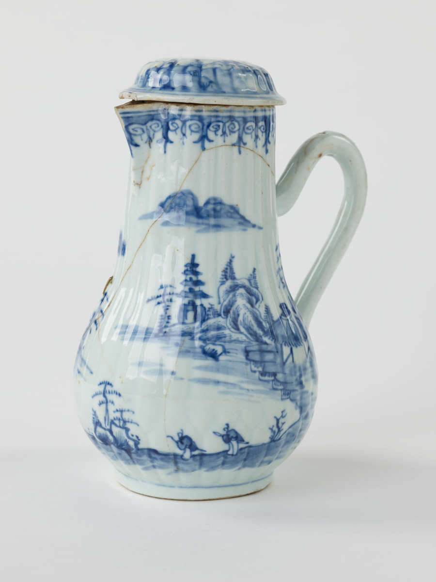 A white chocolate pot with blue decorations depicting floral and architectural elements.