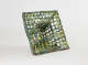 A sculptural, ceramic square form with layers of green and blue mesh, featuring a hollow, square center.