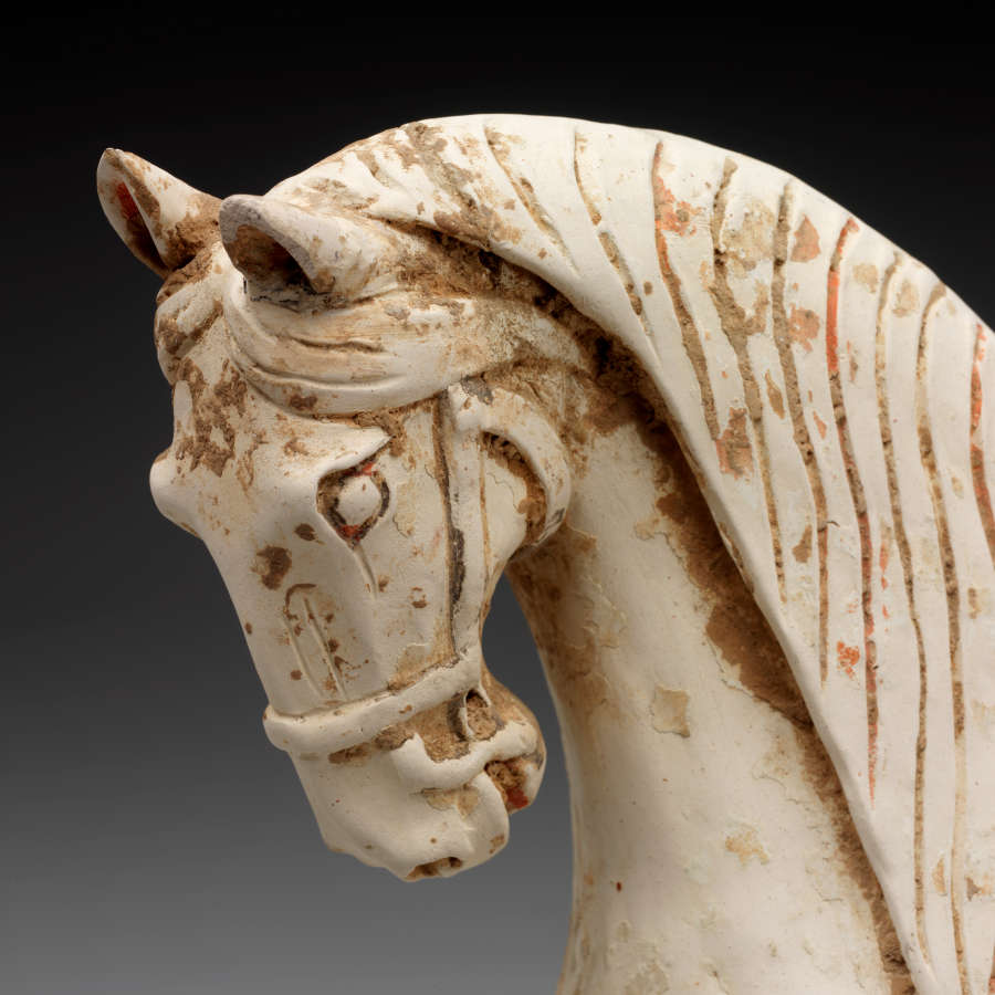 Close-up of the face of a ceramic horse sculpture. Visible are the carvings forming the horse’s facial features, as well as the sculpted ropes wrapped around the horse’s mouth. 