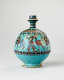 Turquoise jug with a spherical body and slender neck. The jug’s body is decorated with illustrations of winged humanoid four-legged creatures and dark patterned stripes.  It’s handle is not visible.
