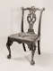 A black and white image of an ornamental wooden chair with an intricate open backrest and an upholstered seat supported by clawed feet.