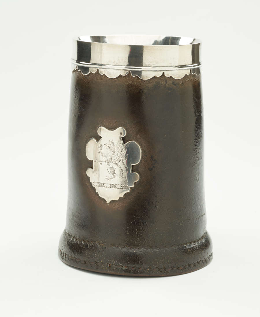 A brown tankard with silver band at top and a decorative silver crest.