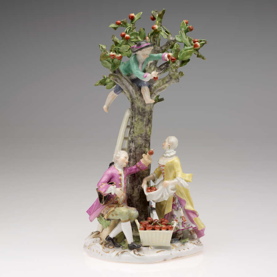  A sculpture with three figures in elaborate historical clothing. One is in the tree while the others stand below next to a ladder and a basket of cherries.
