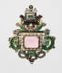 An ornate brooch featuring a central pink gemstone surrounded by enameled decoration in green and black. Two symmetrical dragon heads adorn the sides.
