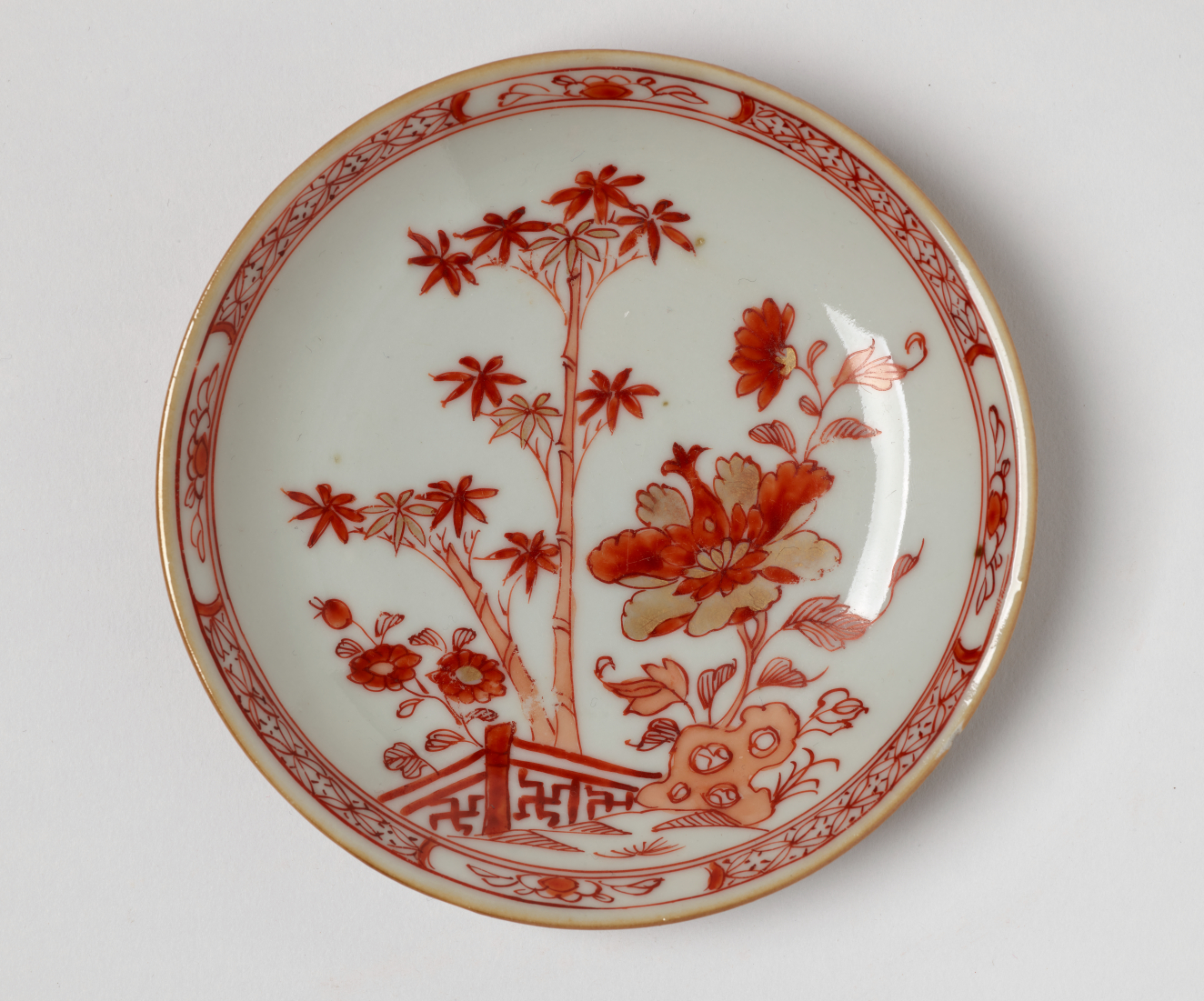  A cream colored plate with red and gold floral, structural, and abstract decorations.