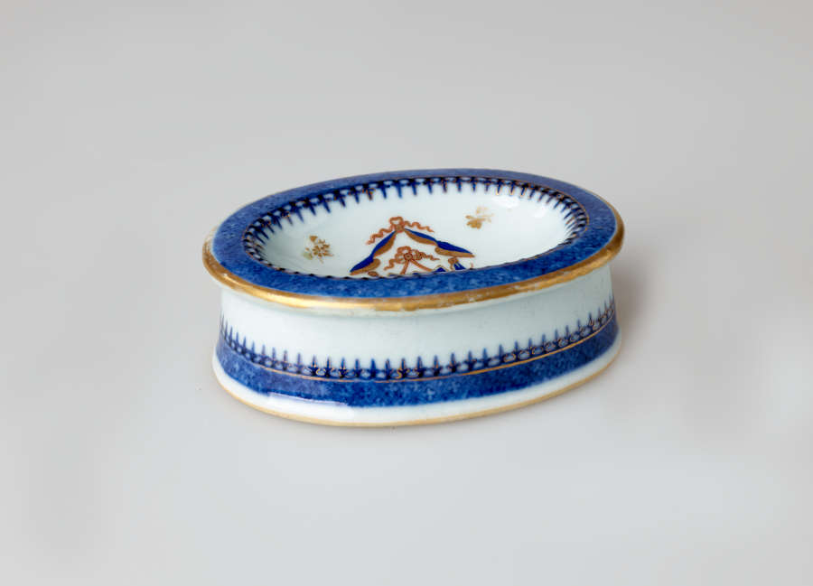 An oval white salt container with blue and gilded decorations.