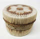 Cylindrical lidded leather box with cross-hatching and linear stripe patterns woven in white and brown straw. The brown rimmed lid has a central floral motif woven atop it.