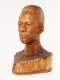 Three quarter front view of a glossy, carved wooden bust depicting the head of a male figure with afrocentric facial features. He has a stern expression and an intense gaze.