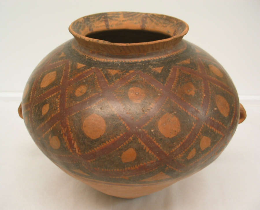 A large, rounded ceramic vessel with a flared rim, decorated with red and black geometric lattice patterns, showing signs of wear and age.