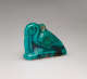 Turquoise amulet at an angle, of a crouching pelican-like bird with a long beak pointed downwards, head tucked into its neck, where there is a small loop. It is labeled in black ‘11.771’.
