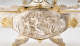 Close-up of a silver oval relief panel depicting a central flowing-robed woman surrounded by playful cherubs and swirling drapery, enclosed in a gold-trimmed frame. 