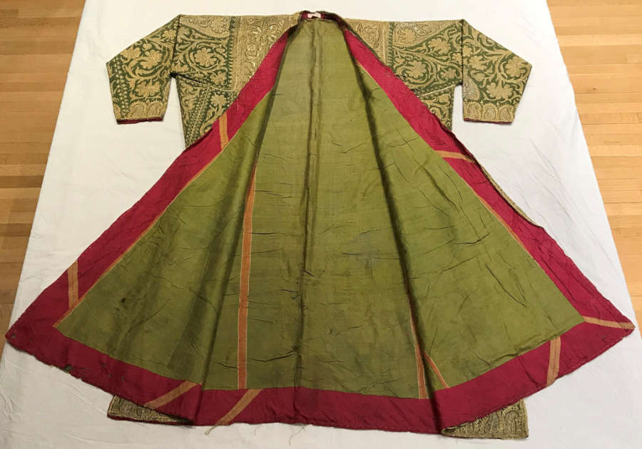 Green coat splayed out on tissue, showing its green lining with a red striped border. Floral patterns have been embroidered on it in gold, its neckline framed with dense embroidery.