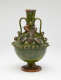 A dark green jug with sculpted decorations, symmetrical decorative handles, and a foot.