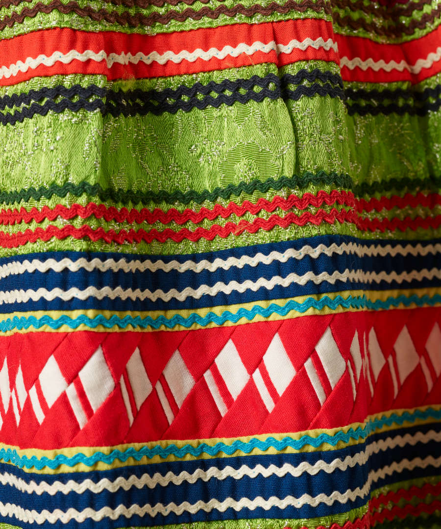 Another detail of the pattern. A thick strip of red with white diamonds woven through it is surrounded by wavy horizontal white, dark blue, dark green, red, and light blue stripes. 