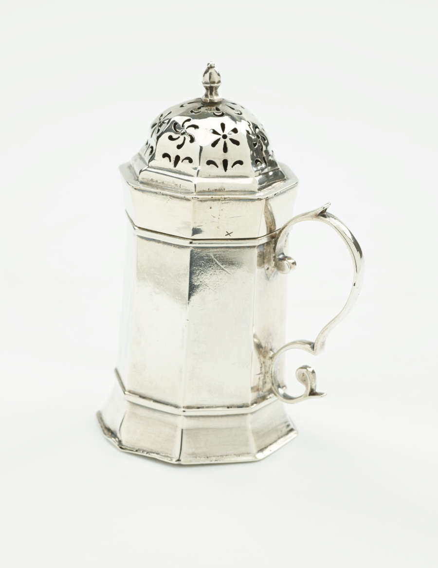  A silver vessel that has an octagonal body, handle, and lid that has floral perforations.
