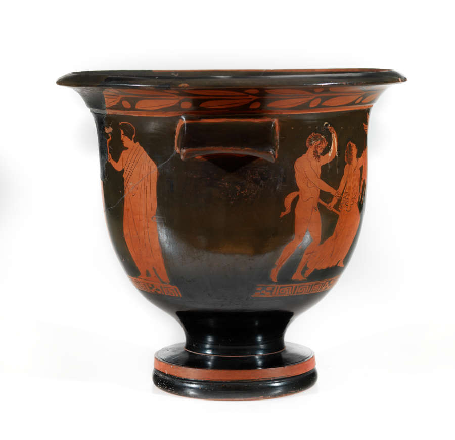 Stout black bowl with a wide striped foot and flared patterned mouth. Visible is one sloping handle, and orange illustrations of figures emerging from  negative space below the handle.