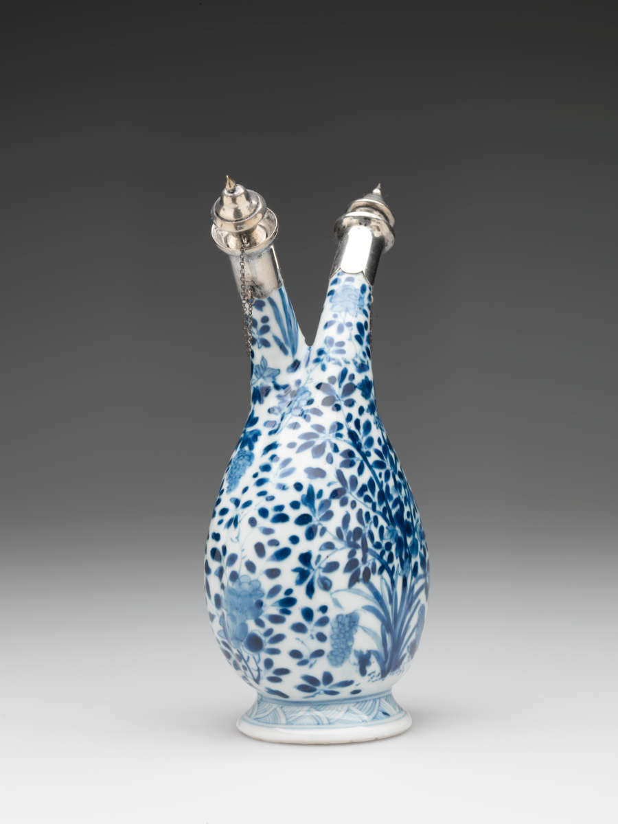 White and blue vessel with a flared foot, rounded body, and two necks in opposite directions. Necks are closed with silver caps attached to the vessel with delicate chains.