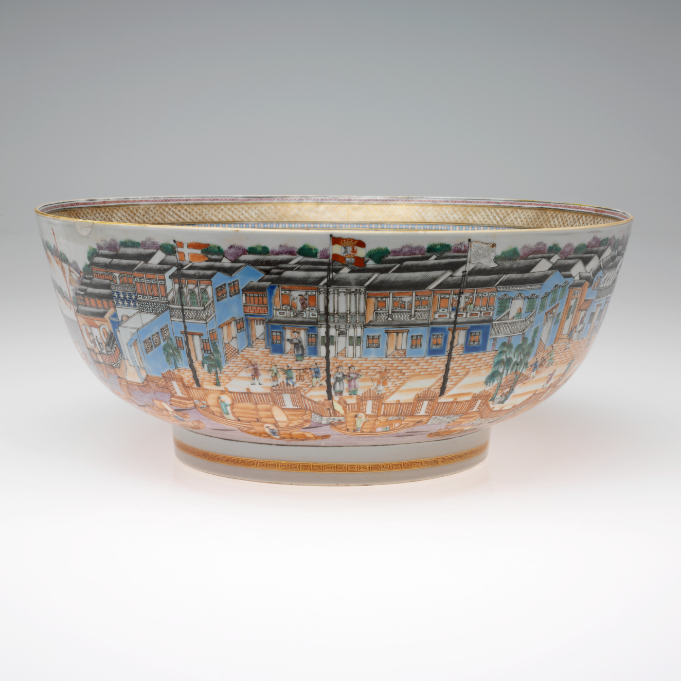 An intricately painted ceramic bowl with a bustling city scene, featuring colorful buildings, trees and figures, and including a gold rim.