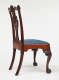 A side view of an antique wooden chair with an intricately carved backrest and a blue upholstered seat with claw shaped feet and curved legs.