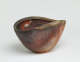 Side-angle view of a speckled brown clam-shaped bowl. Its rim dips at its sides to form a wavelike shape along the top. Its warm, earthy surface features shell-like etchings. 