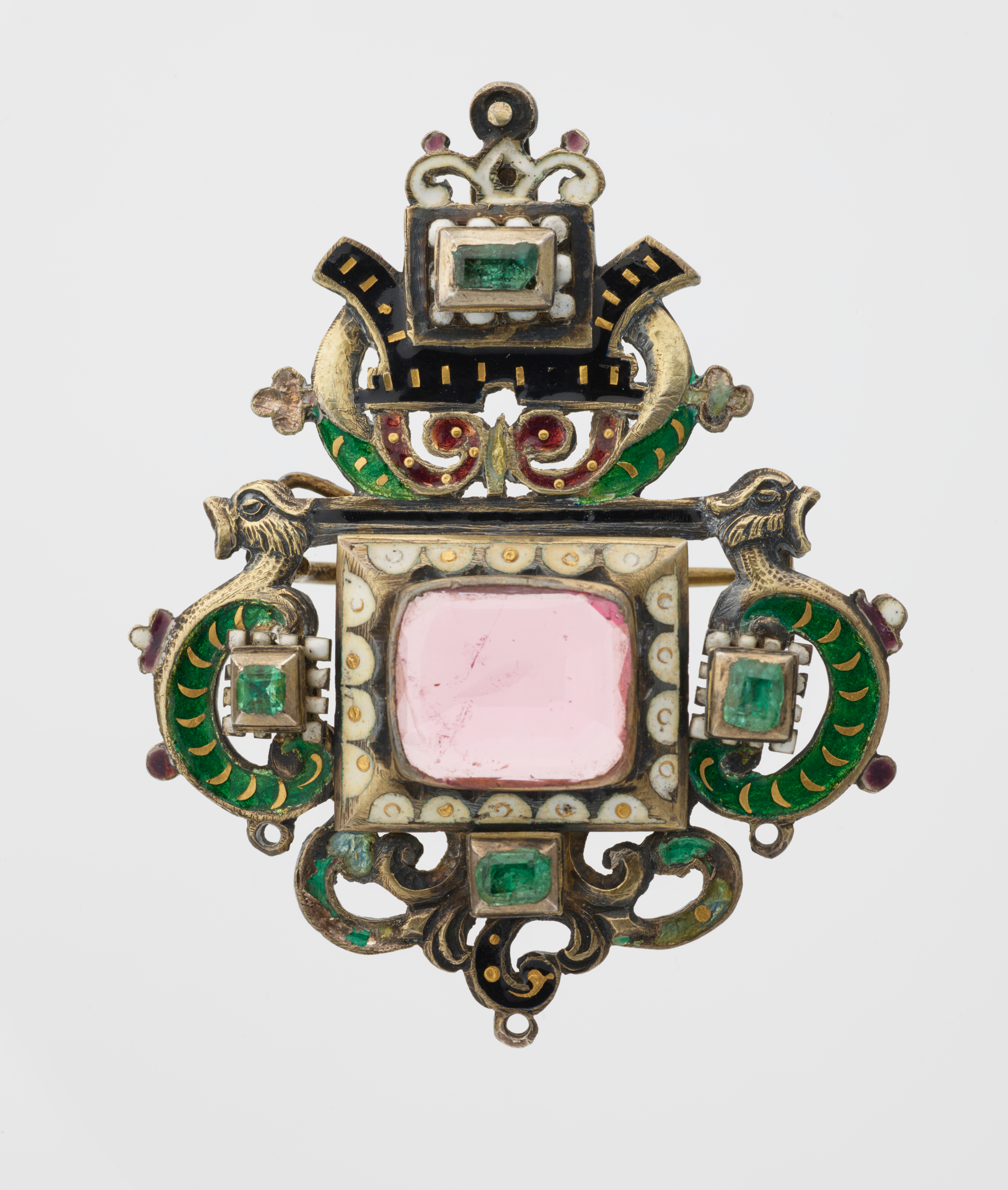 An ornate brooch featuring a central pink gemstone surrounded by enameled decoration in green and black. Two symmetrical dragon heads adorn the sides.