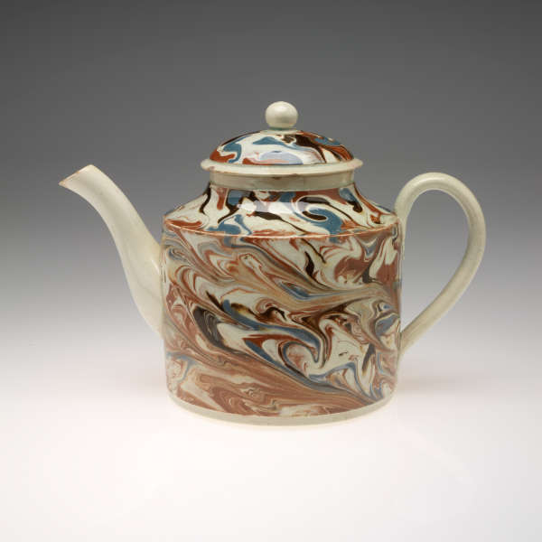 Teapot with a swirling, marbled design on the body and lid in brown, blue, black, and cream. Spout, handle, and rounded finial are solid cream colored.