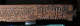 Side view of a carved wooden panel with interlocking triangular patterns and a calligraphic inscription at the right end. 