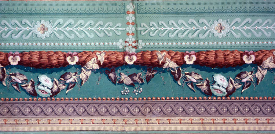 Elegant and botanical border design of floral swags hanging from wheat sheaves against a patterned sage green backdrop. Ornamental patterns line the bottom trim of the design.