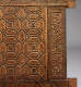 A close up of a wooden panel with repeating geometric designs, bordered by calligraphic inscriptions along the right edge. 