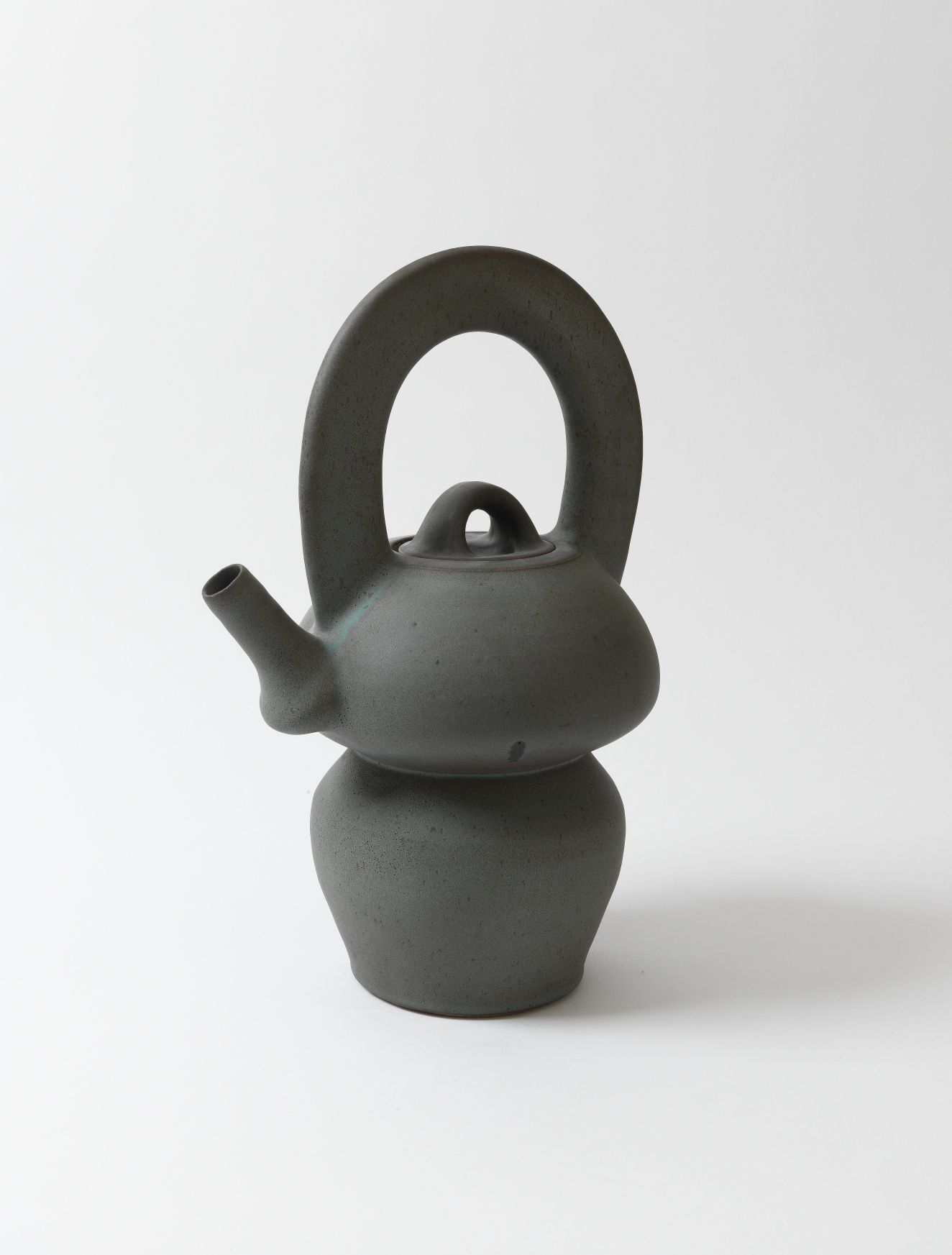A smooth, minimalistic dark gray teapot with a smooth matte surface, bulbous upper and lower sections joined by a narrow waist, and an oversized handle looping above the lid.