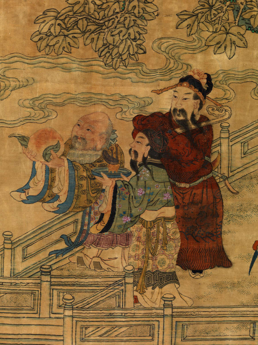 Detail of the scroll showing two three robed figures standing together with their hands raised to the left. The leftmost man holds up a large peach. They are on a balcony amongst leaves and clouds.