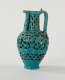 A turquoise ewer with cut out decorations and a sculptural spout and handle.