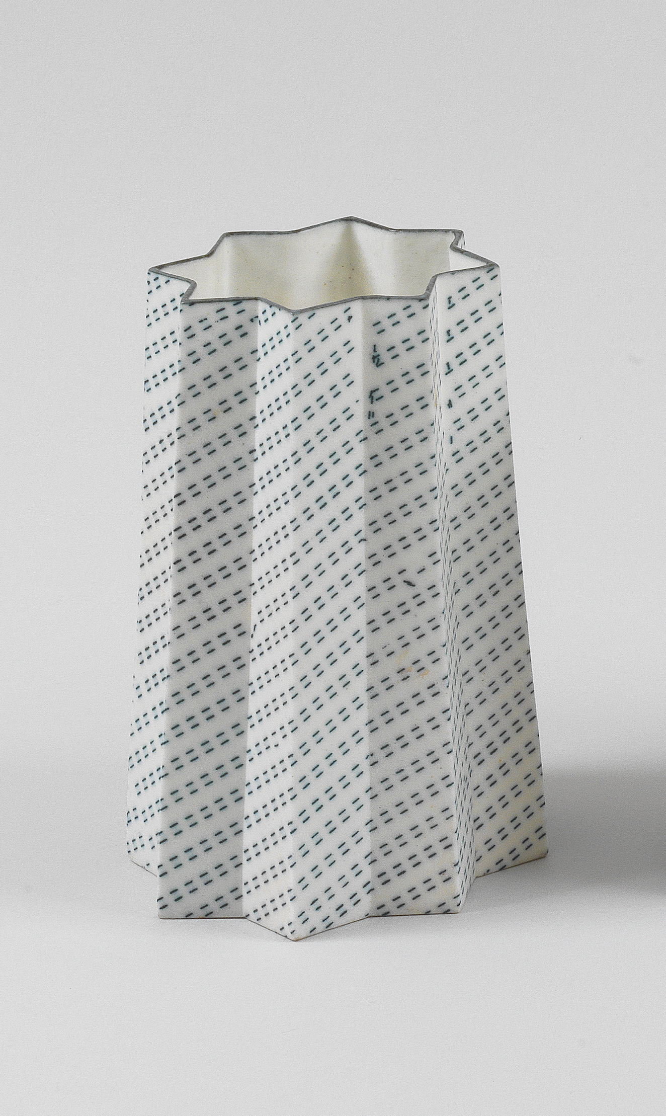 A tall, star-shaped vessel with eight points, its panels decorated with diagonal rows of dashes and black that wrap around the structure. 