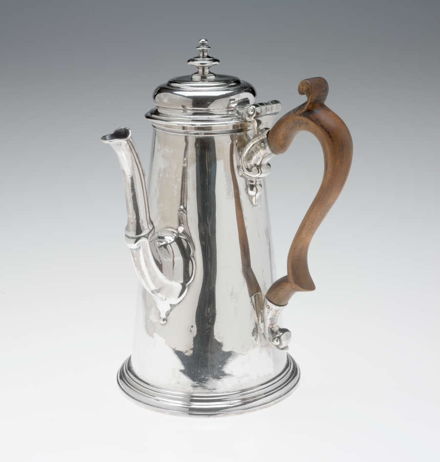 A silver chocolate pot with a spout, hinged lid, and fruitwood handle that is 90 degrees from the spout.
