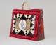Rectangular leather and fur bag with red beaded border, central white circle with red-outlined seal silhouette, black geometric fur pattern, and a side panel with a vibrant red-orange seal.  