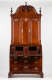 A tall standing cabinet made of polished mahogany wood with intricate metal handles on the lower drawers, fan-shaped carvings on the upper panels, and a rounded top featuring a curving inset.