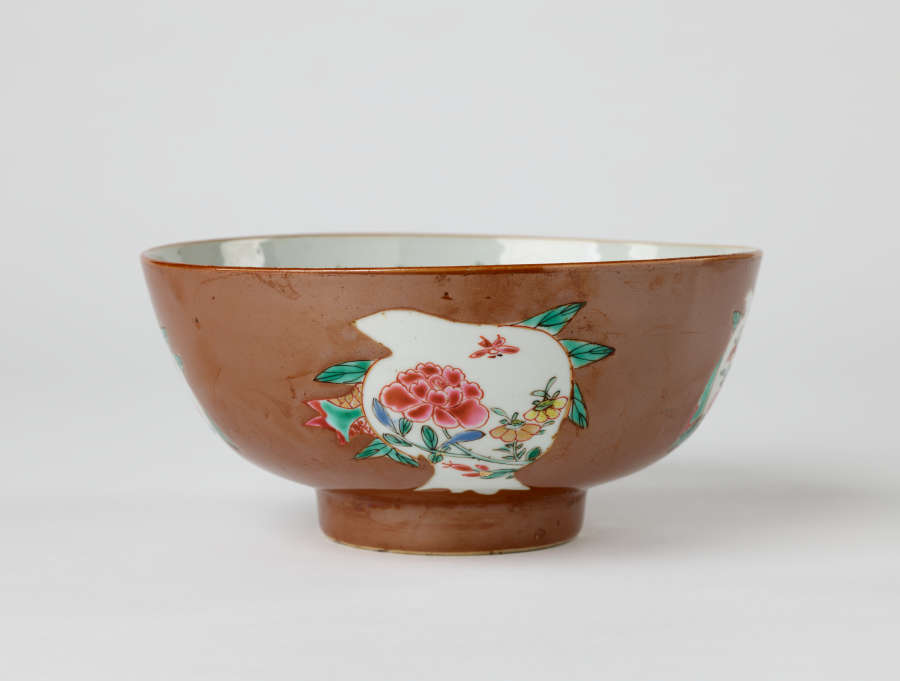 A white and brown bowl with green, yellow, and pink floral decorations with a short, small foot.