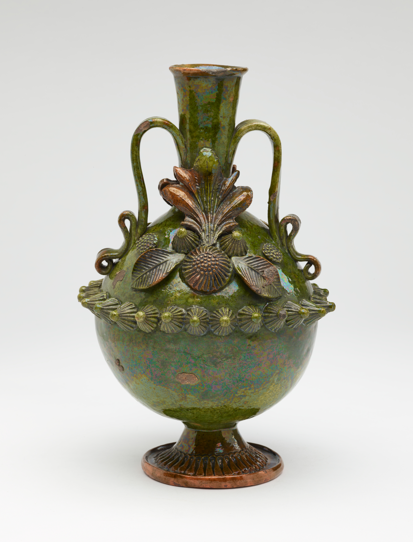A dark green jug with sculpted decorations, symmetrical decorative handles, and a foot.