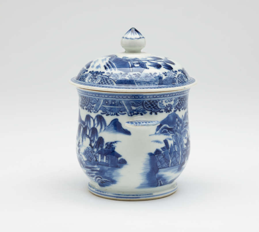 A white bowl with flat handles and lid. The blue decorations are architectural and floral.