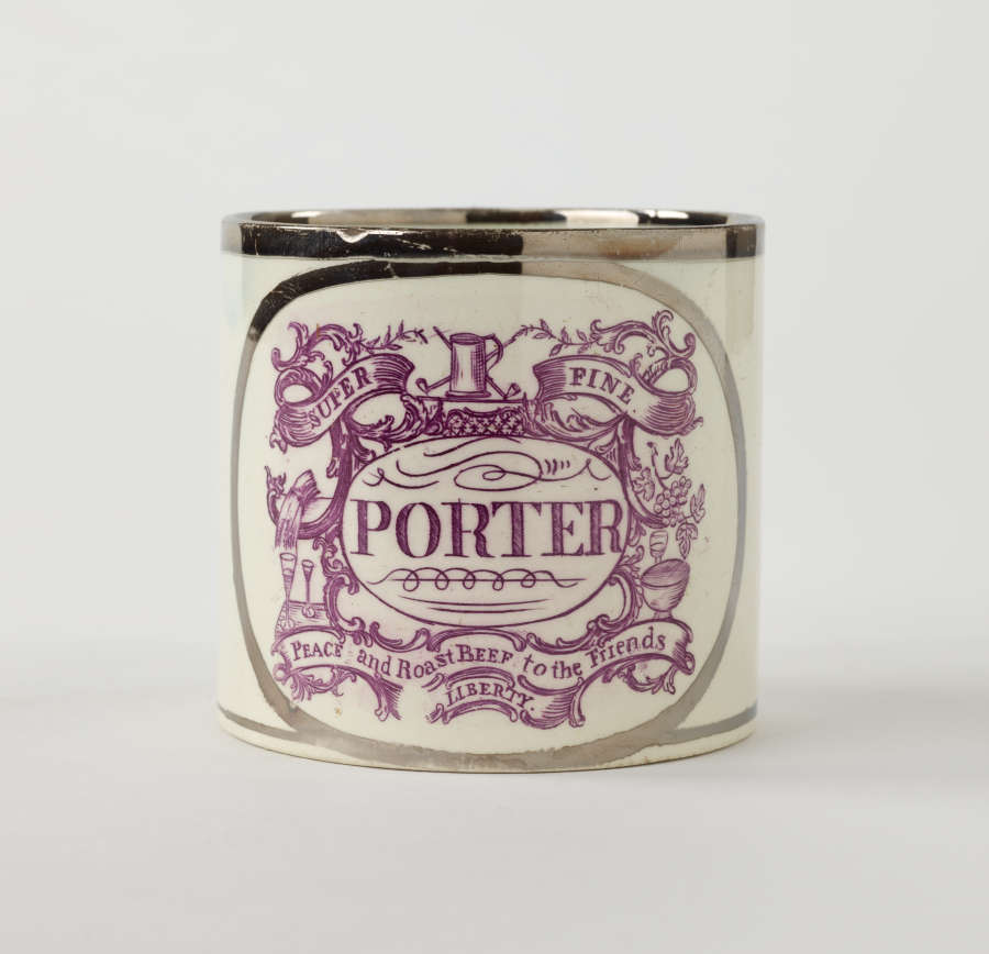 A white mug with silver colored rim and dark purple, swirling decorations. Text on the front reads, “Super Fine Porter. “Peace and Roast Beef to the Friends Liberty.”