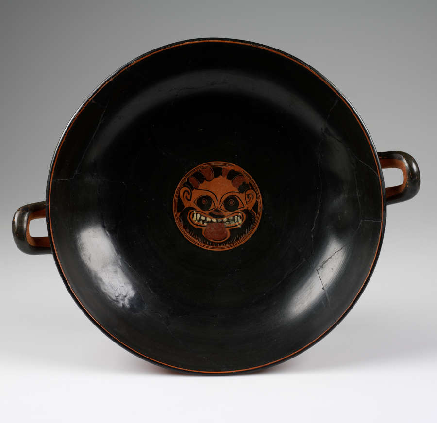 Top view of a cup with a wide mouth showing two handles peeking out from the edges. Its interior is glossy black with a terracotta illustration of an animal face.